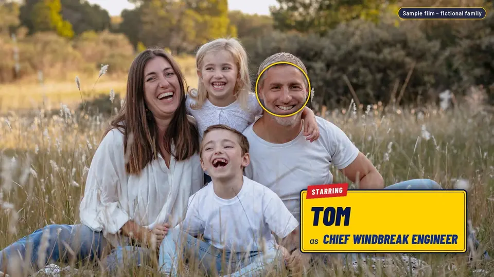 Family portrait in a sunny grassy meadow with a yellow rental-sticker cast card: Starring Tom as Chief Windbreak Engineer